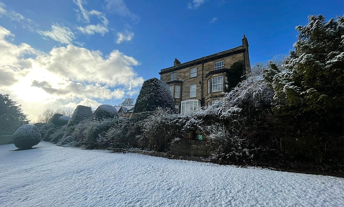 A stone school building and gardens covered in snow under a bright blue winter sky.