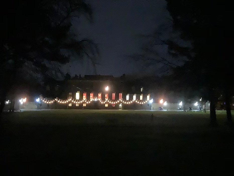 A large building illuminated by string lights at night, with trees and a dark sky in the background.