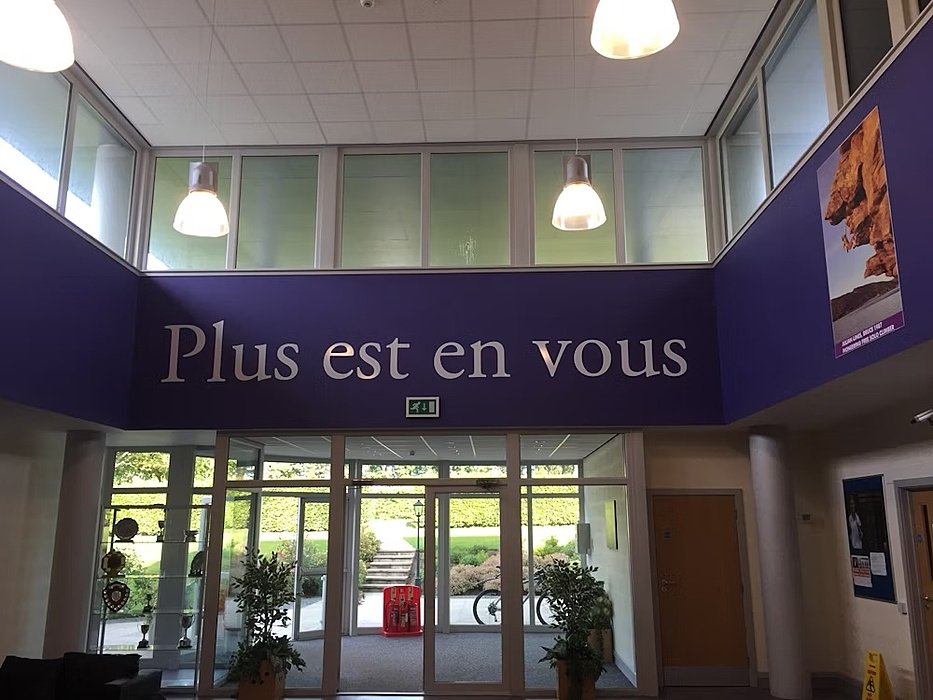 Hallway, over the glassdoors is a blue banner with white text "Plus est en vous"