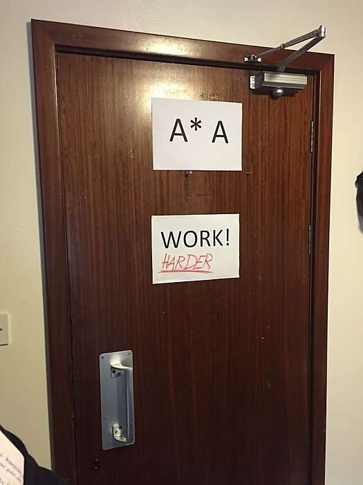 A dark wooden door with two white sheets that say A*A and WORK! Harder