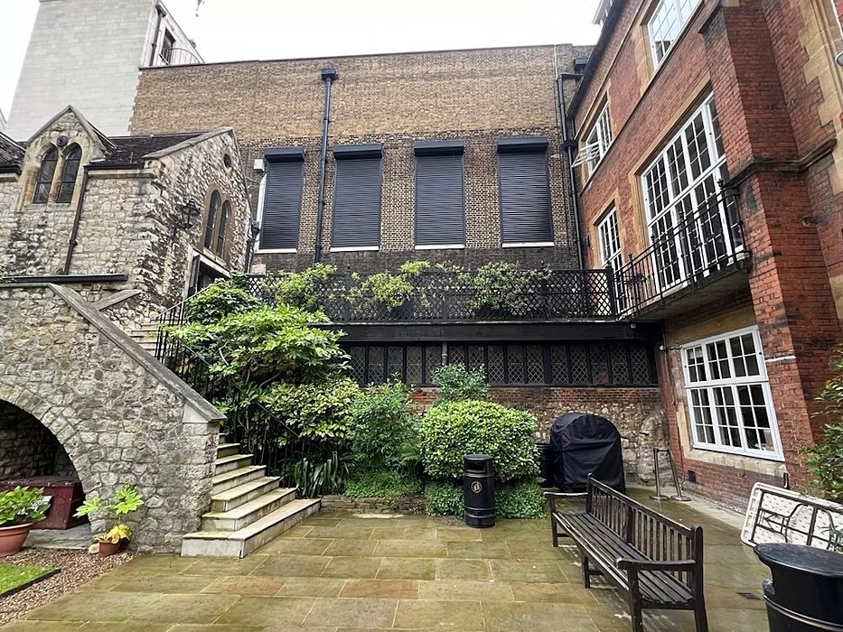 Stone courtyard with stairs leading up to brick and stone buildings covered in greenery.