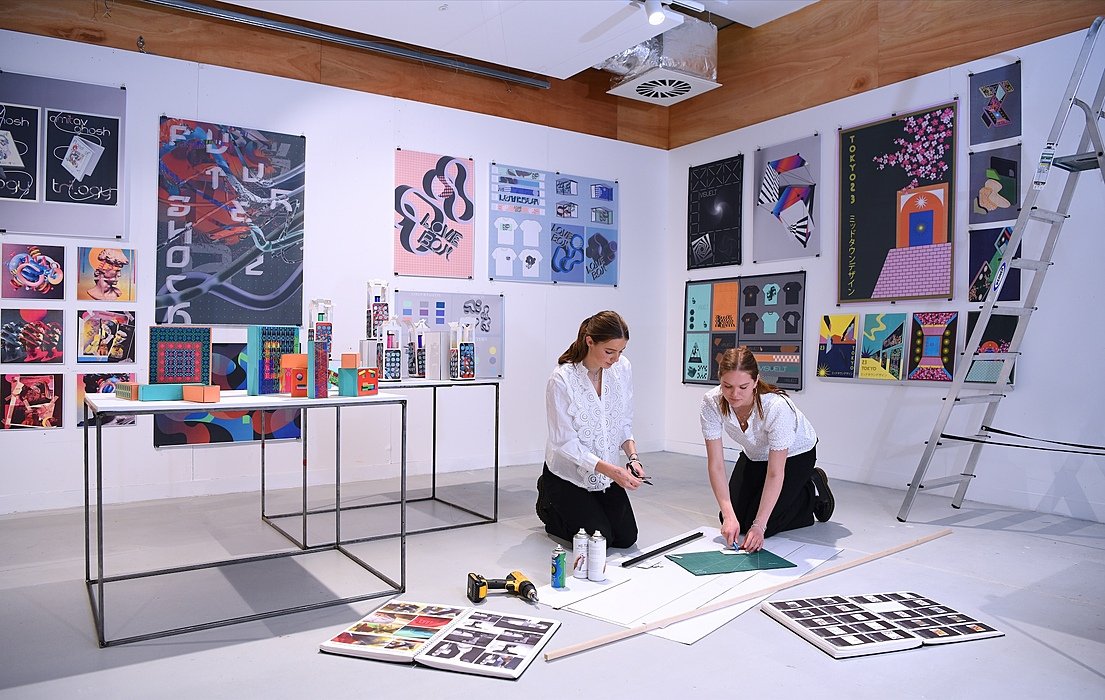 Two female students in white shirts kneeling on the floor doing some artwork