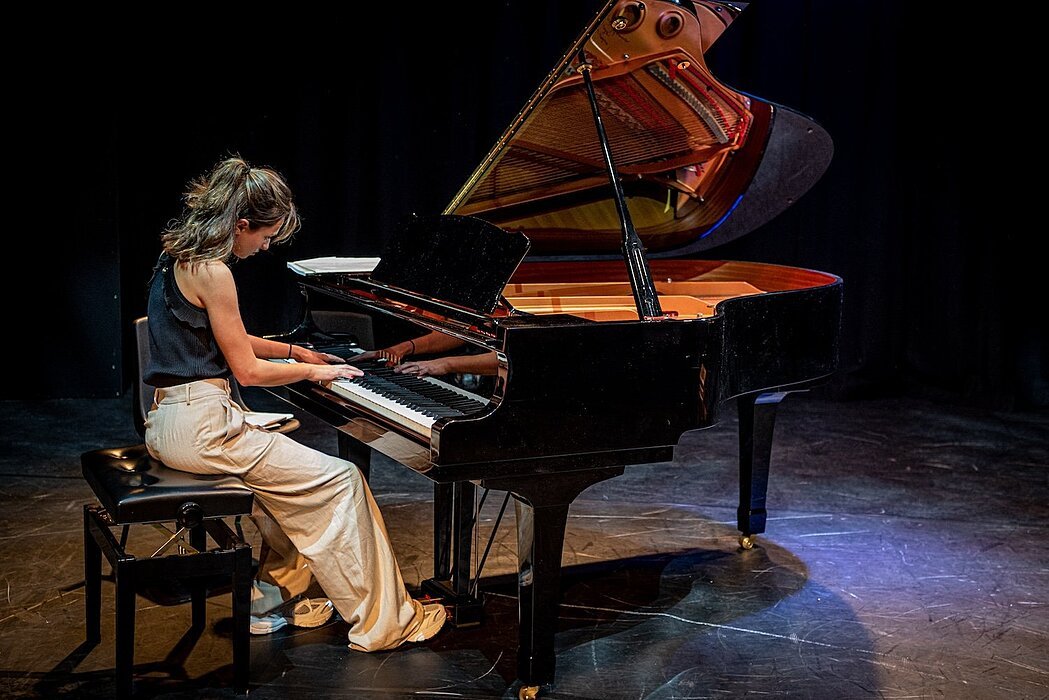A student performing a piano solo on stage in a dimly lit auditorium.