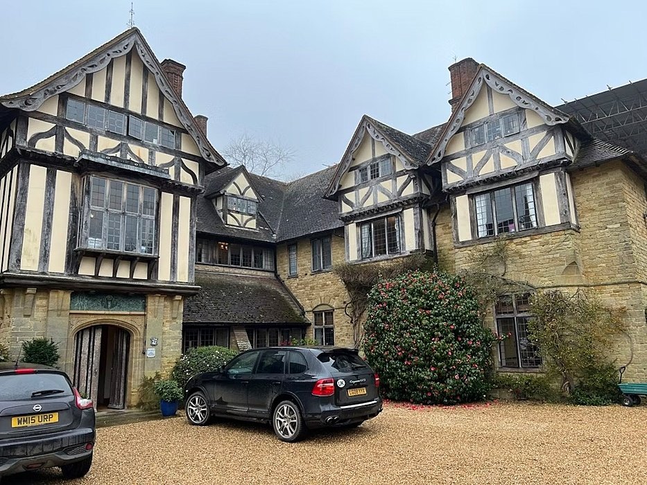 Tudor-style building with timber framing and stone walls, with cars parked in the courtyard.