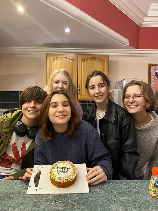 Five girls celebrating a girl's birthday with cake in a boarding house kitchen