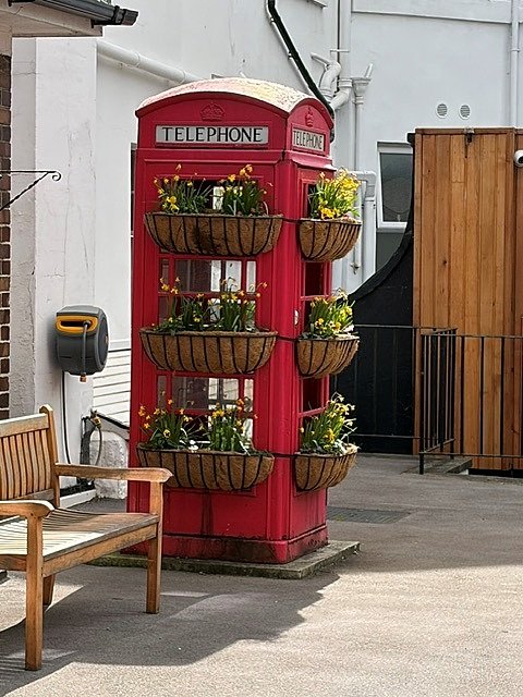 A red British telephone box is used as a flower display, with several planted baskets.