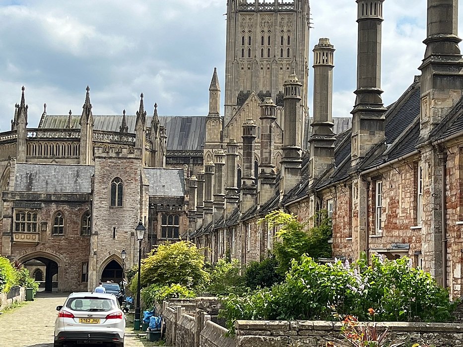 Row of old stone houses leading to a grand cathedral with towers and detailed Gothic architecture.