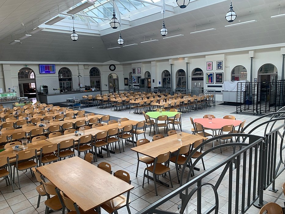 Large dining hall with long tables beneath a glass roof