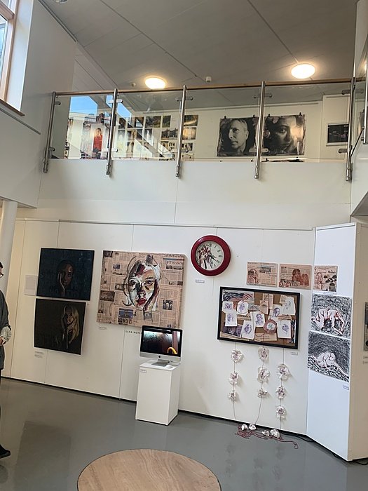 A two-storey gallery displaying photographs, drawings and a red wall clock.