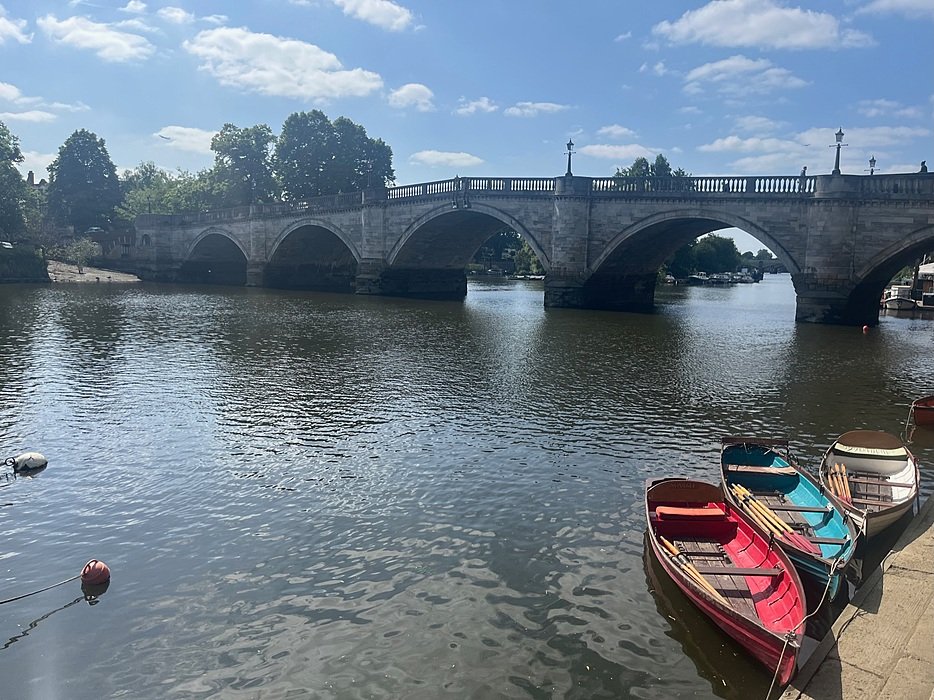 a bridge with round arches over a river with colorful wooden boats tied up in the in the foreground