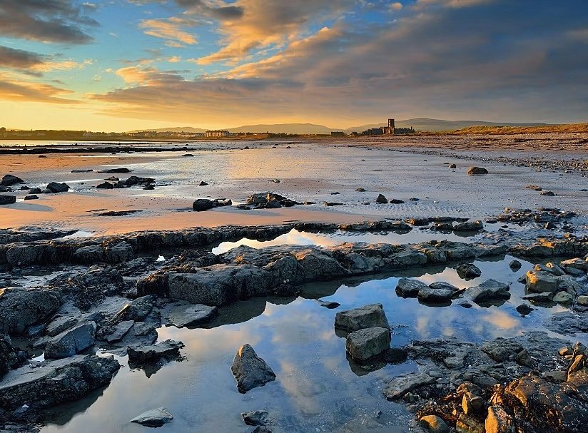 Tide on the beach, lots of rocks and sand and a blue organge sky with clouds