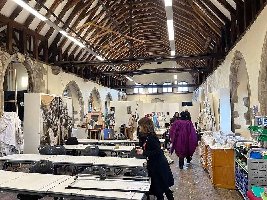 The art department with rows of desks and chairs between old stone archways and under a wooden ceiling