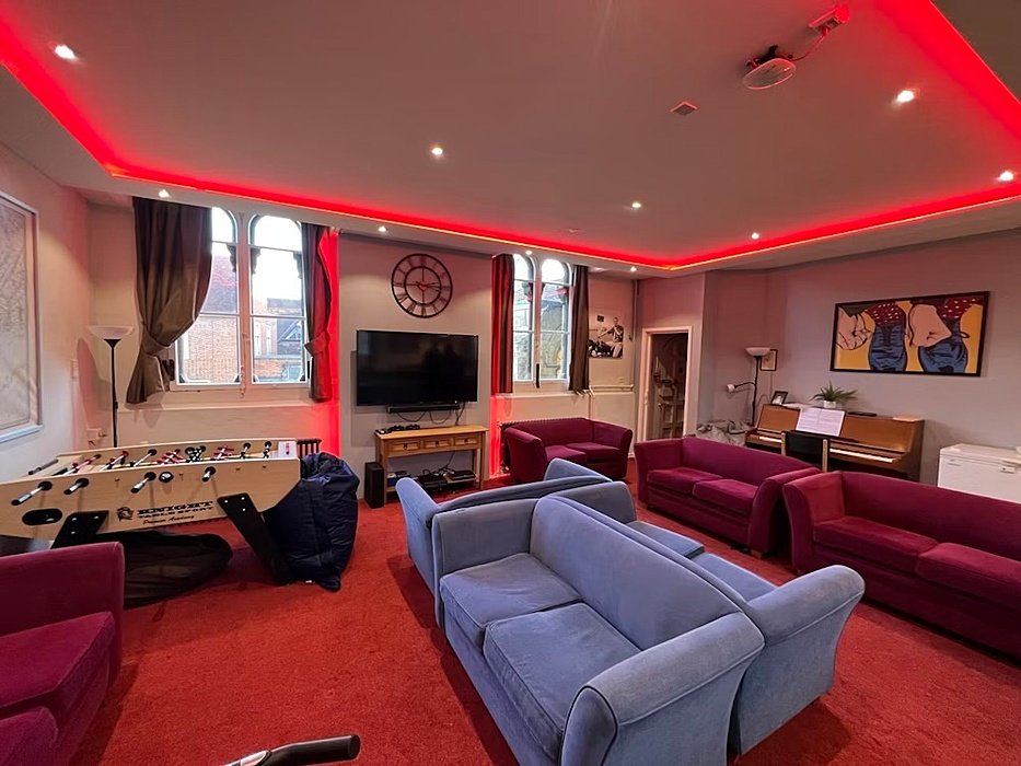 A living room in a boarding house with football table, piano, comfy sofas and TV