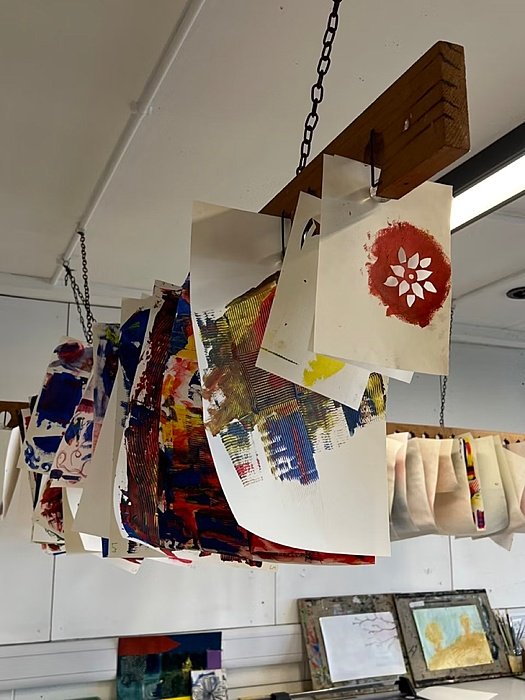 A drying rack hanging from the ceiling with dozens of pieces of art drying on it
