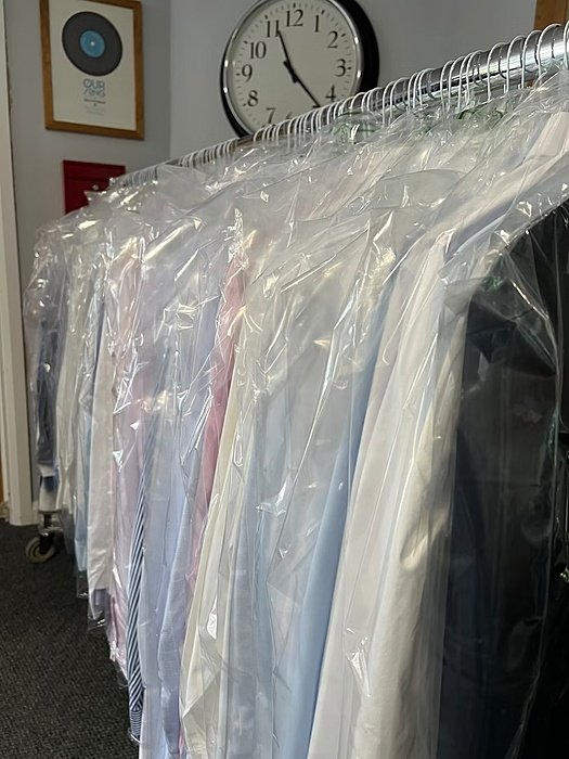 freshly washed and ironed shirts wrapped in plastic hanging on the rail ready for pick up