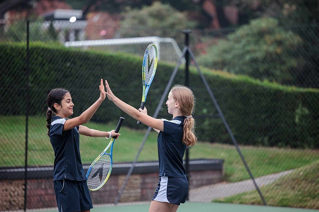 Two girls dressed in tennis jerseys, holding rackets, high-fiving each other