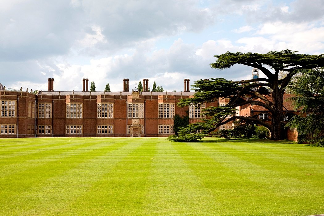 Historic brick school building with a large lawn and mature tree in the foreground.