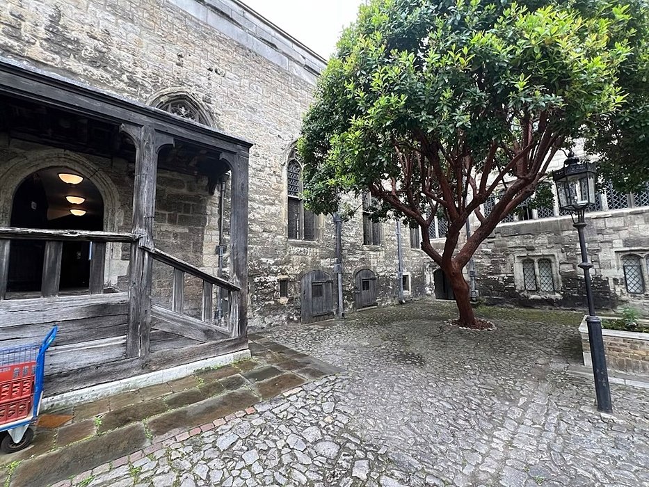 Small stone courtyard with a large tree and old wooden porch entrance.