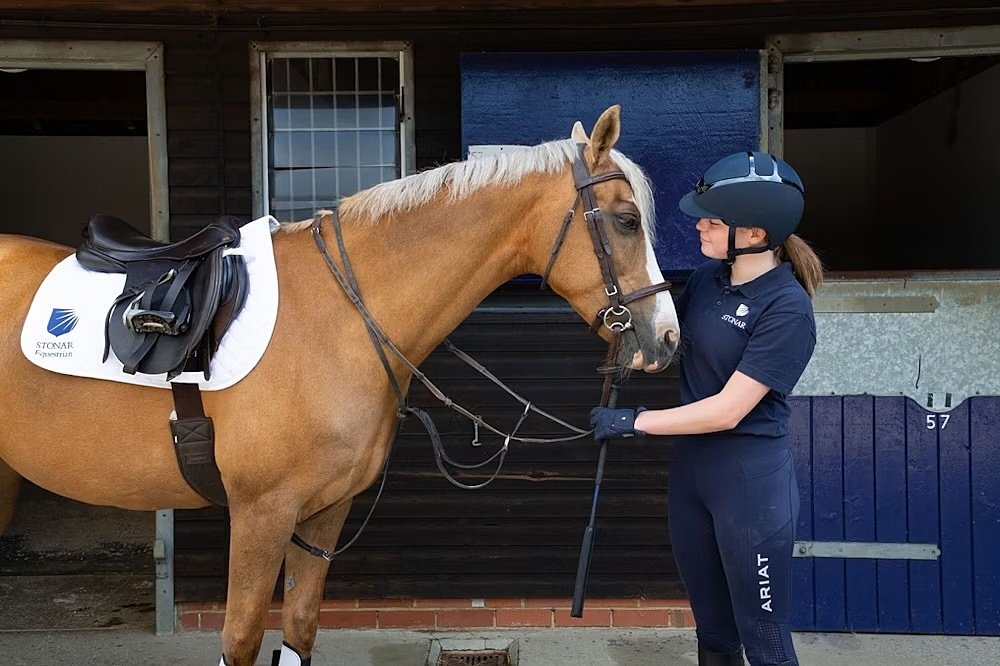 A student in her riding gear is standing face to face with her horse holding the bridle
