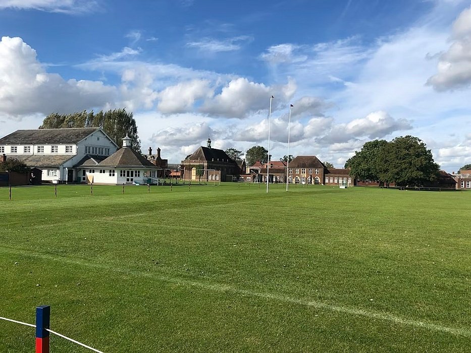 Rugby field surrounded by traditional brick buildings under a blue sky with clouds.