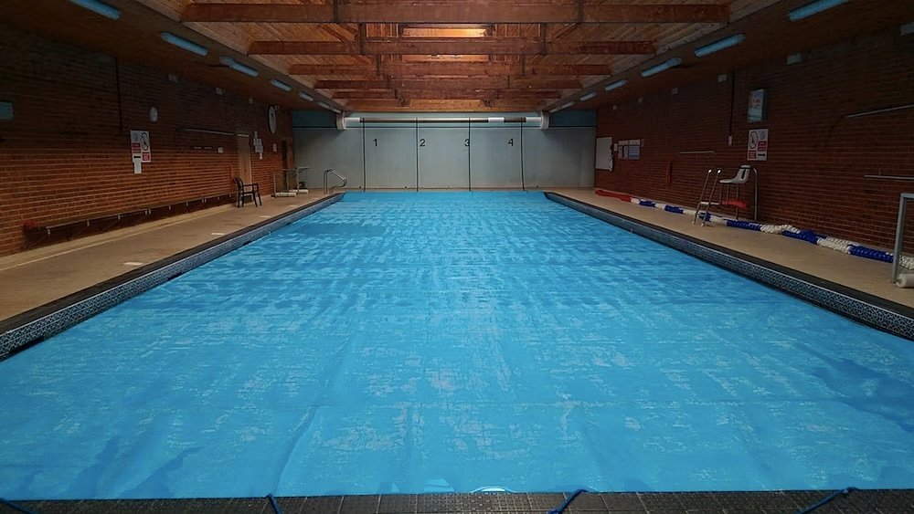 Indoor swimming pool with blue pool cover and brick walls under a wooden ceiling.