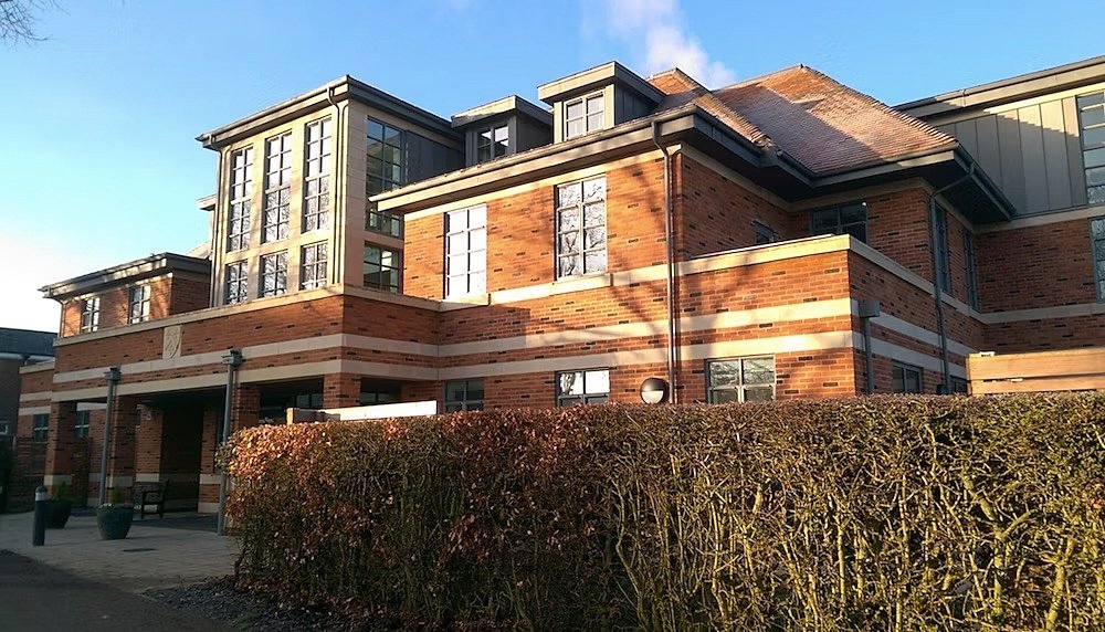 Modern red-brick school building with large windows and a neatly trimmed hedge.