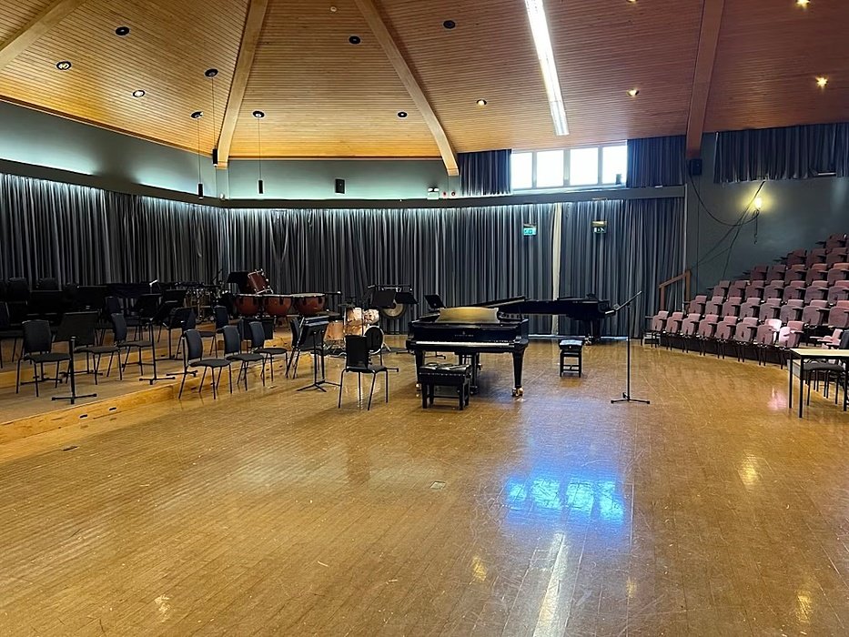 A piano on stage in a high-ceilinged auditorium, with chairs for the orchestra and rows of seats for the audience.