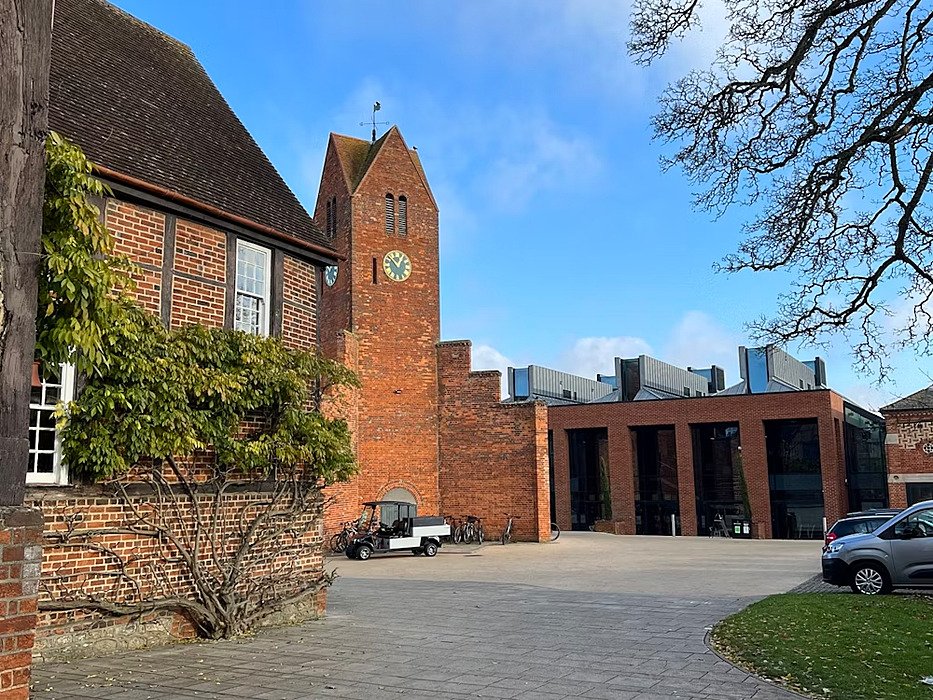 a brickstone tower with a clock, some cars and a courtyard