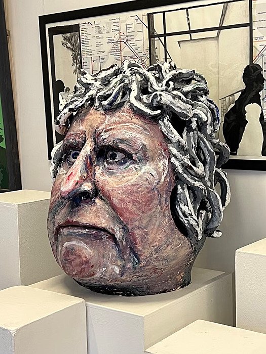 Bust of a large head with thick, worm-like hair, a fixed stare, pointed nose, and downturned mouth