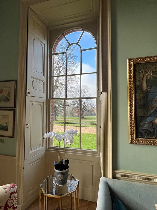 Elegant old room with interior shutters opening to a garden view, and a small table with a flower in front of the window