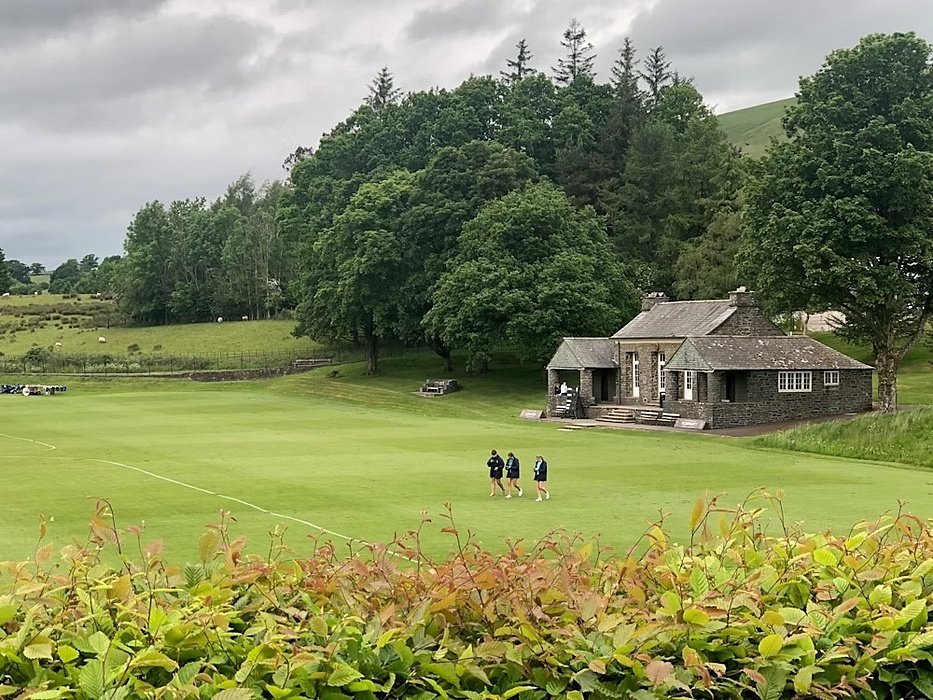 Sportsfield with a small grey house and trees