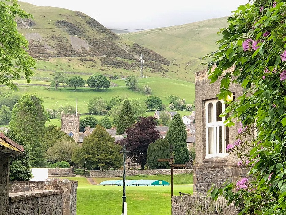 view between some school buildings onto the cricket pitch and the rolling hills in the background