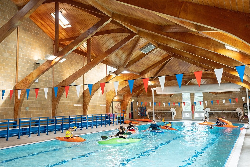 A beautiful indoor swimming pool with wooden beams and students in canoes on the water