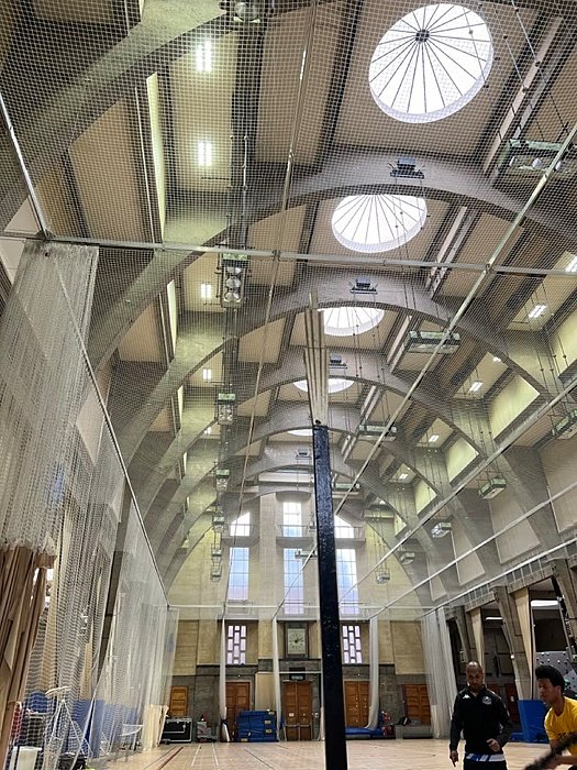 Large indoor sports hall with high arched ceiling, skylights, and cricket nets.