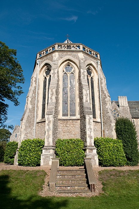 Historic stone chapel with tall arched stained-glass windows and decorative stonework, surrounded by greenery under a clear blue sky.