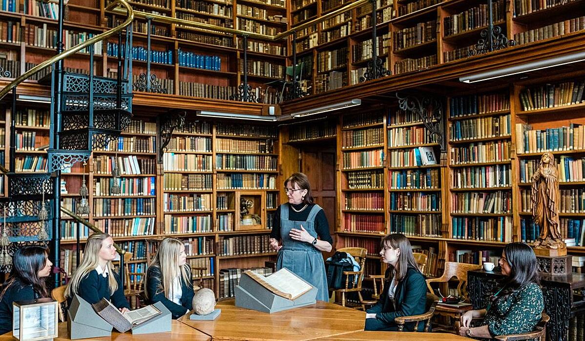 a teacher with her students in an old library with books up to the ceiling and iron spiral stairs leading up