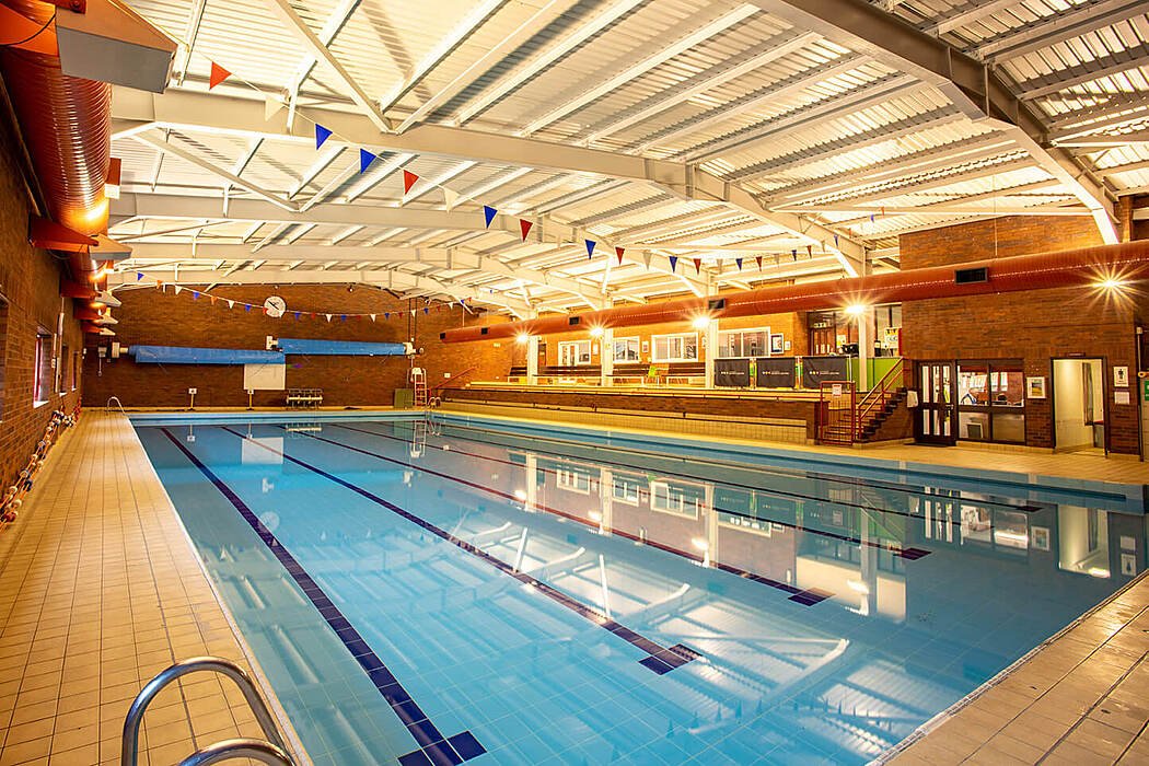An indoor swimming pool with lanes and spectator seating, lit by bright ceiling lights in a brick-walled facility.