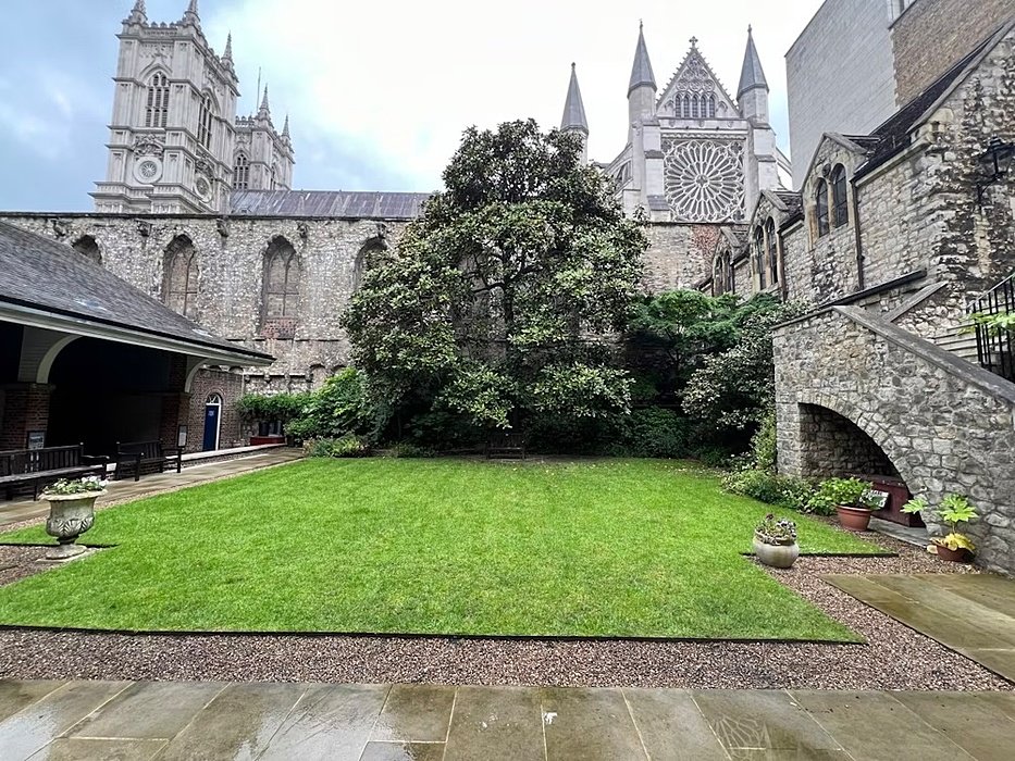 Courtyard garden with neatly cut grass, surrounded by historic stone buildings and cathedral towers in the background.