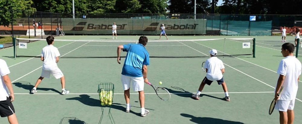 Group of students practicing tennis on outdoor courts under sunny weather.