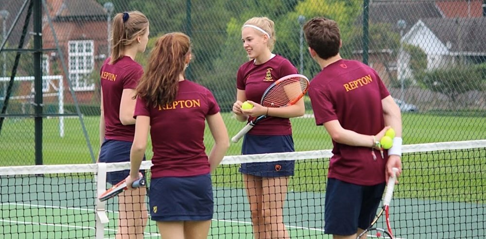 Group of students wearing matching Repton uniforms standing on a tennis court and talking.