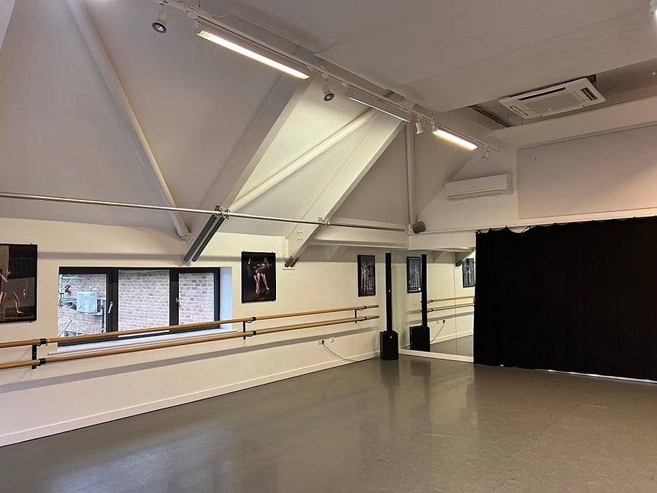 Bright dance studio with mirrored walls, ballet barres, and framed photos of dancers.