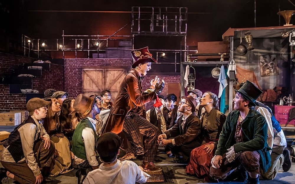 Scene from musical Oliver, boy singing, others in dirty clothes sitting around him
