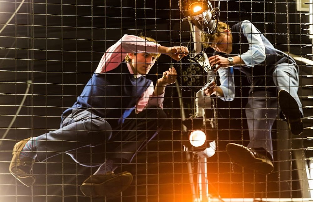 Two men hanging in a grit, fixing lights in a theatre