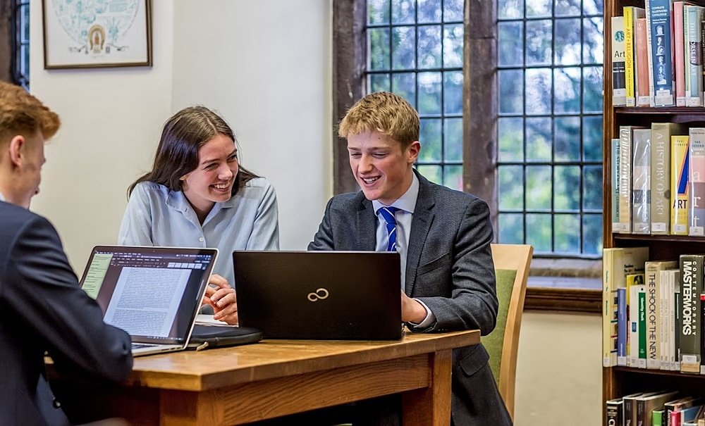 Three students at a library table with laptops