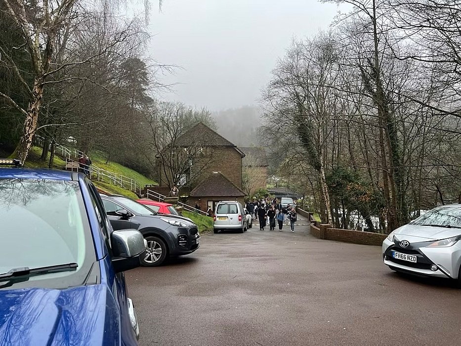 Students walking up a hill through a misty wooded campus car park with parked cars.