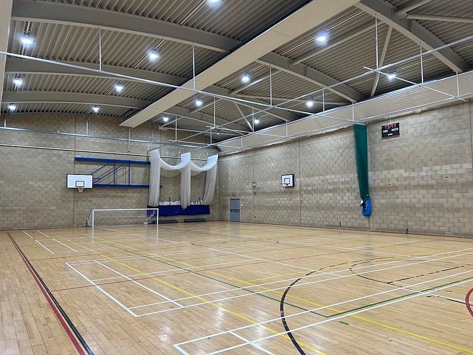 A large indoor sports hall with wooden flooring, basketball hoops, and court markings.