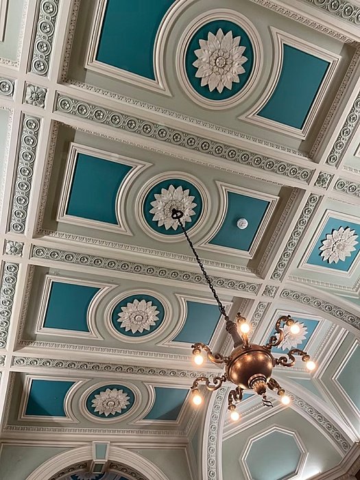 A beautifully decorated ceiling with teal panels, white floral motifs, and a chandelier.