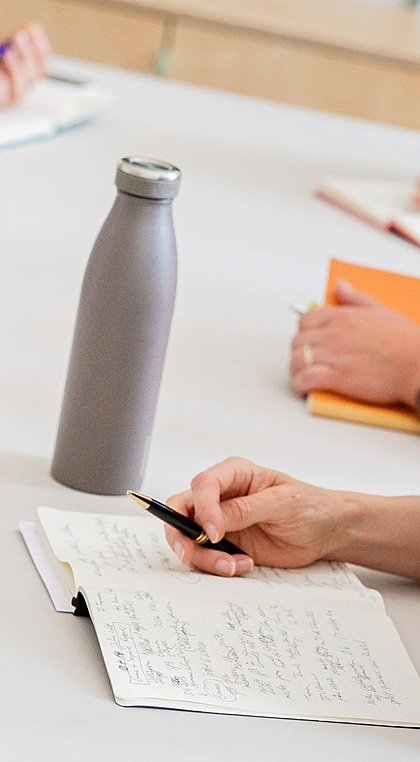 A close-up shot of table, on which a bottle, laptop and hands of people are visible