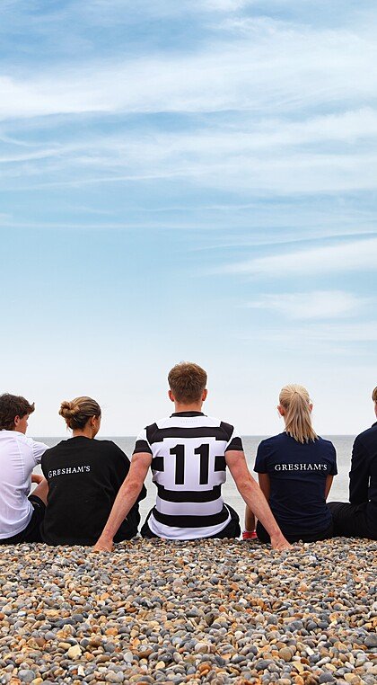 Gresham's School pupils sitting on a pebbly Norfolk beach