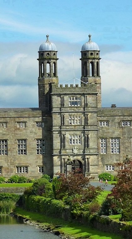A large historic stone building with twin domed towers, surrounded by landscaped gardens and a reflecting pond.